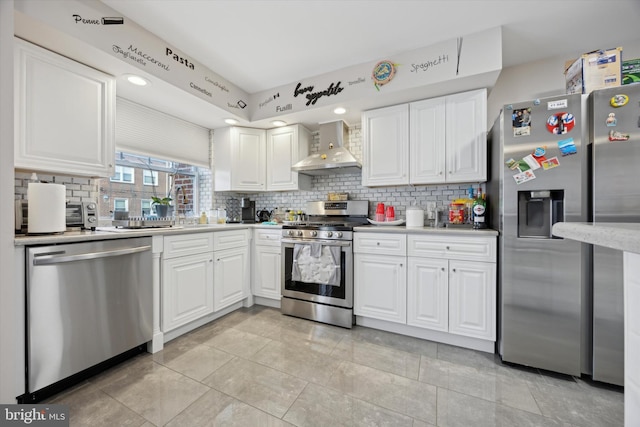 kitchen featuring backsplash, white cabinets, wall chimney exhaust hood, light tile patterned floors, and stainless steel appliances