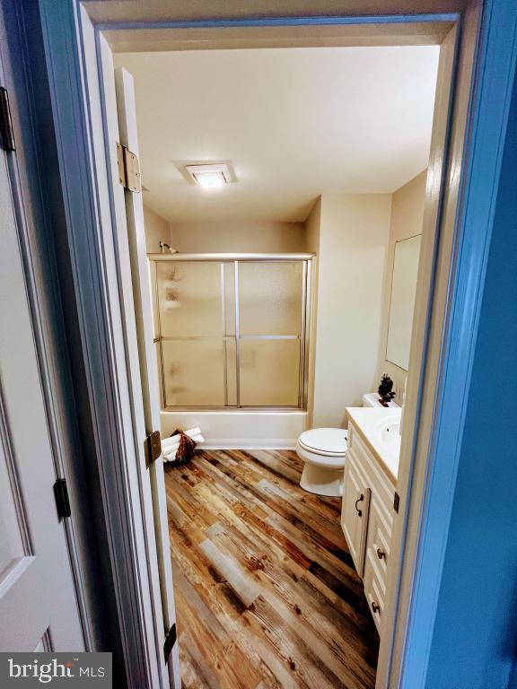 full bathroom with hardwood / wood-style flooring, vanity, toilet, and combined bath / shower with glass door