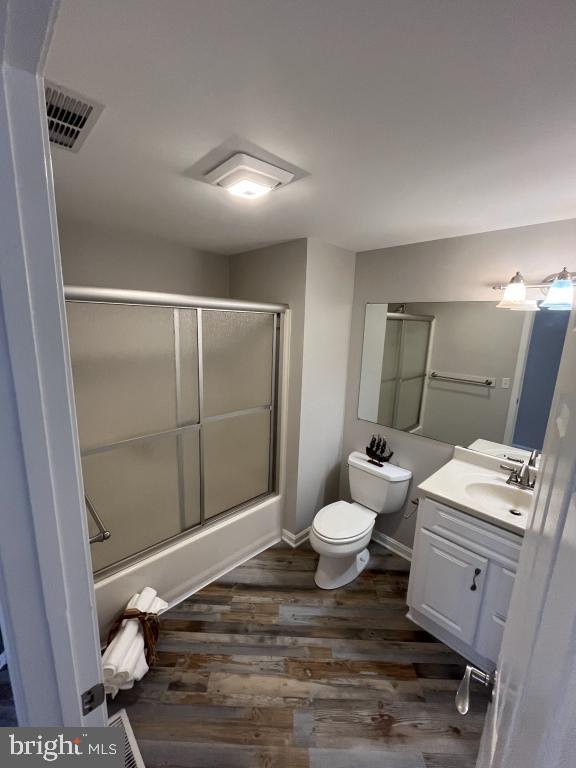 full bathroom featuring shower / bath combination with glass door, wood-type flooring, vanity, and toilet