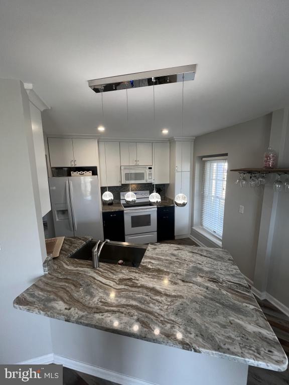 kitchen with white appliances, white cabinets, sink, stone countertops, and kitchen peninsula