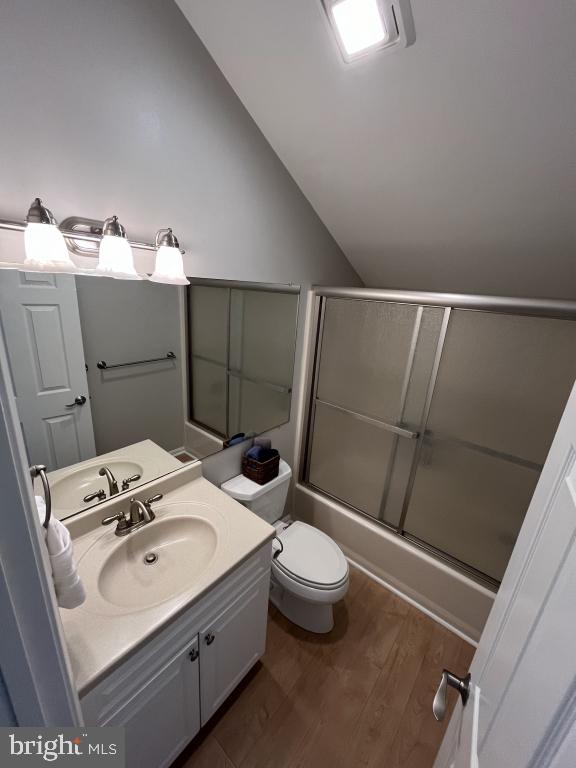 full bathroom featuring bath / shower combo with glass door, vanity, vaulted ceiling, wood-type flooring, and toilet