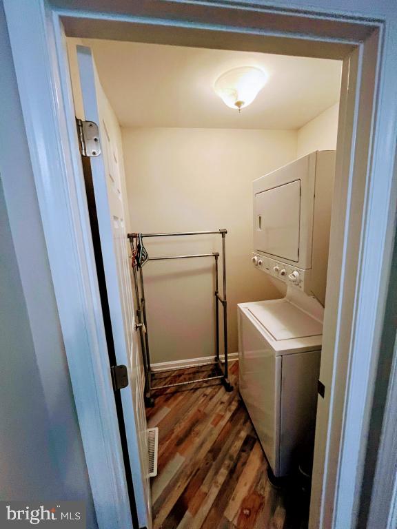 laundry area featuring dark wood-type flooring and stacked washer and clothes dryer