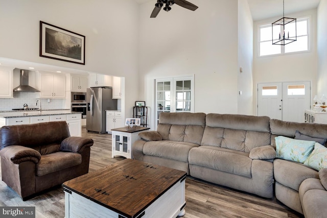 living room with a high ceiling, ceiling fan with notable chandelier, hardwood / wood-style flooring, and french doors