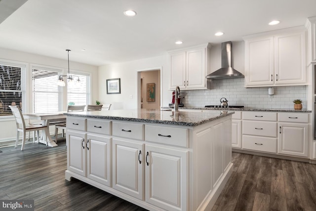 kitchen with a center island, wall chimney range hood, dark hardwood / wood-style floors, decorative backsplash, and white cabinetry