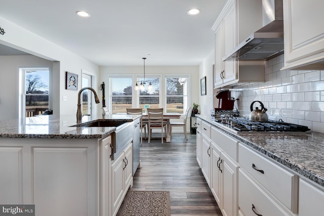 kitchen with a kitchen island with sink, plenty of natural light, dark wood-type flooring, and wall chimney range hood