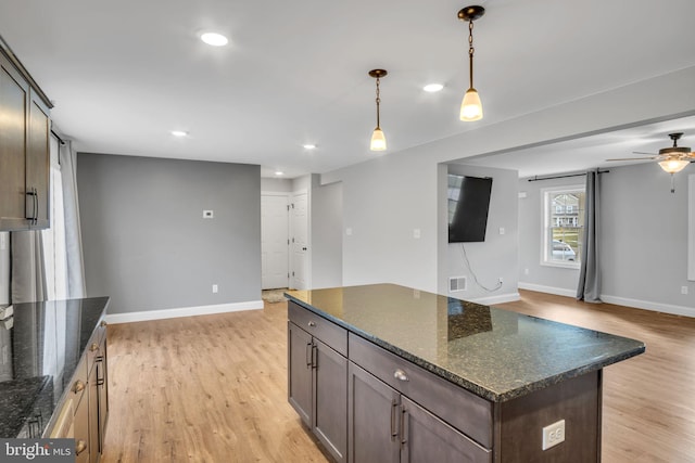 kitchen featuring dark brown cabinets, light wood-type flooring, hanging light fixtures, and dark stone counters