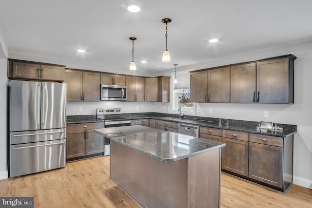 kitchen featuring light hardwood / wood-style flooring, dark stone counters, pendant lighting, a kitchen island, and appliances with stainless steel finishes