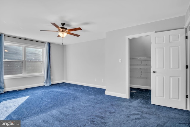 unfurnished bedroom featuring ceiling fan, dark carpet, a walk in closet, and a closet