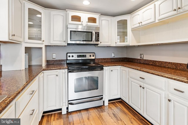 kitchen featuring light wood-type flooring, white cabinetry, dark stone countertops, and appliances with stainless steel finishes