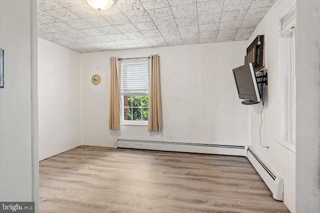 empty room featuring light wood-type flooring and a baseboard heating unit