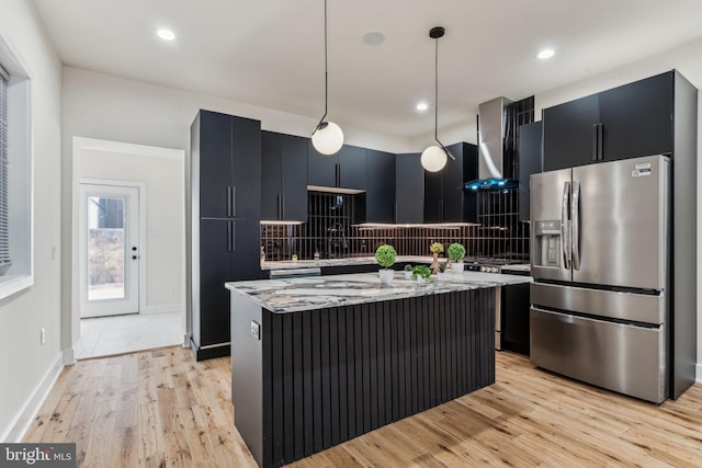 kitchen with wall chimney exhaust hood, light hardwood / wood-style flooring, stainless steel fridge with ice dispenser, a kitchen island, and hanging light fixtures