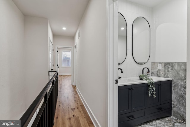 hall featuring light wood-type flooring, tile walls, and sink