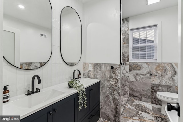 bathroom with vanity, toilet, and tile walls