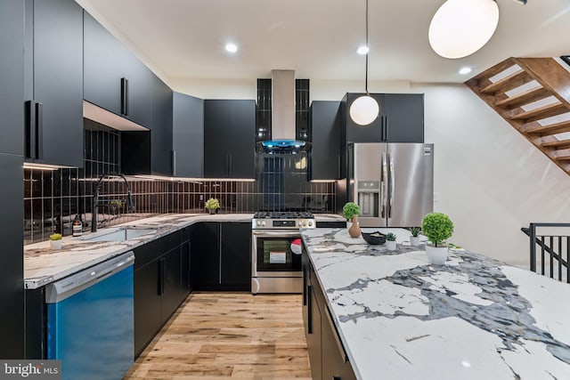 kitchen with appliances with stainless steel finishes, light wood-type flooring, backsplash, wall chimney exhaust hood, and decorative light fixtures