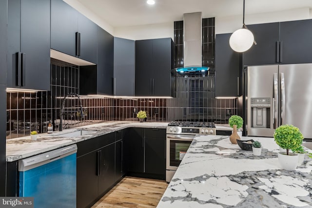 kitchen featuring wall chimney range hood, hanging light fixtures, decorative backsplash, light hardwood / wood-style floors, and stainless steel appliances