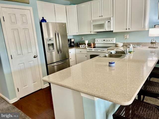 kitchen with kitchen peninsula, sink, white appliances, white cabinetry, and a kitchen breakfast bar