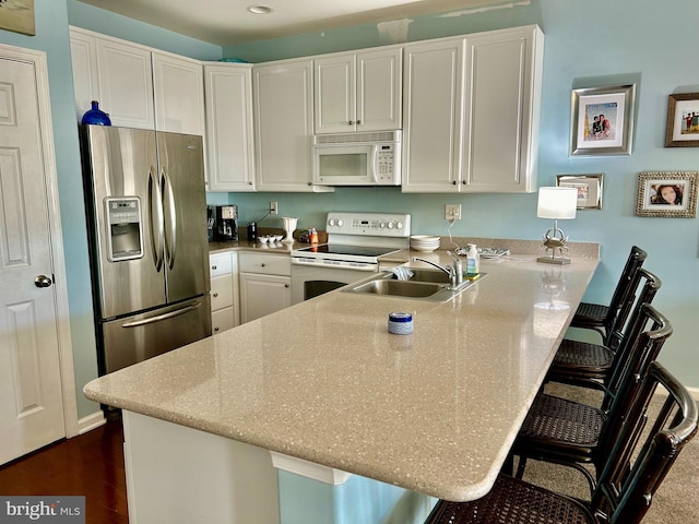 kitchen with a breakfast bar area, sink, kitchen peninsula, and white appliances