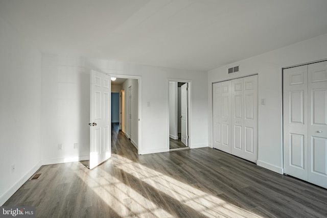 unfurnished bedroom with two closets and dark hardwood / wood-style floors