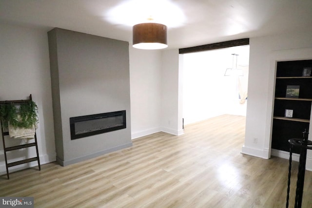 unfurnished living room with built in shelves and light wood-type flooring