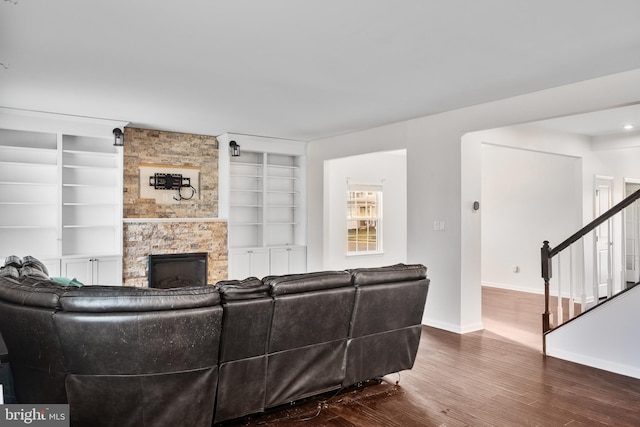 living room featuring wood-type flooring, a stone fireplace, and built in shelves