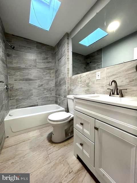 full bathroom with vanity, tiled shower / bath, a skylight, toilet, and tile walls