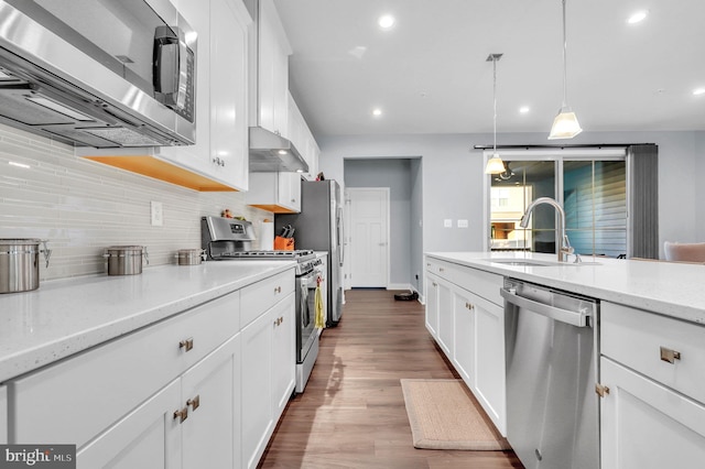 kitchen with hardwood / wood-style floors, white cabinets, sink, hanging light fixtures, and stainless steel appliances