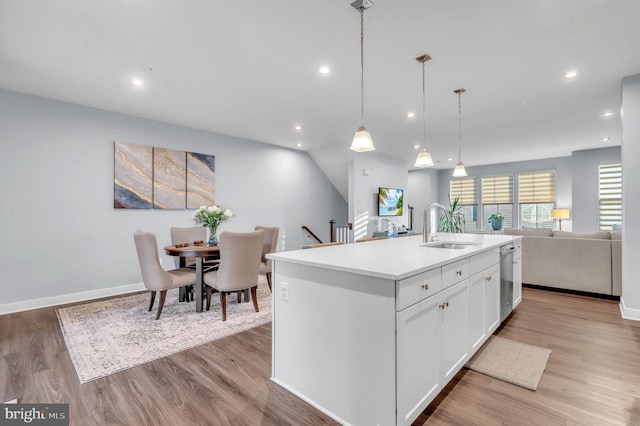 kitchen with sink, light hardwood / wood-style flooring, an island with sink, decorative light fixtures, and white cabinets