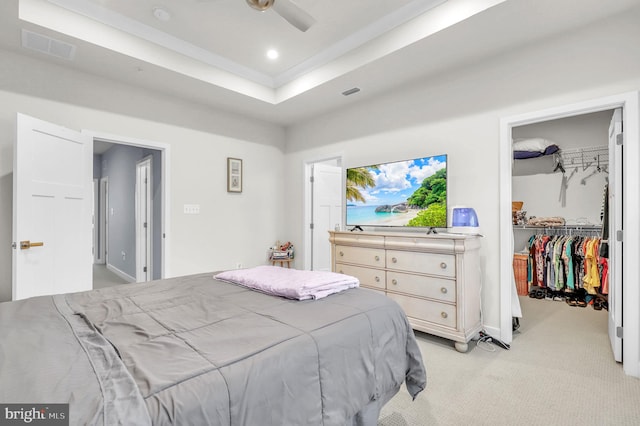 carpeted bedroom with a raised ceiling, ceiling fan, a closet, and a spacious closet