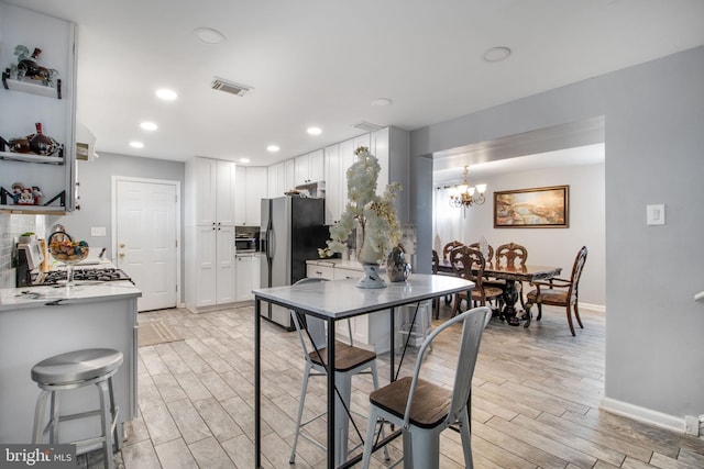 kitchen featuring hanging light fixtures, light wood-type flooring, white cabinetry, stainless steel appliances, and a chandelier