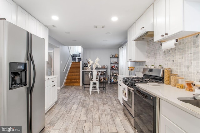 kitchen with white cabinets, appliances with stainless steel finishes, light wood-type flooring, and light stone countertops