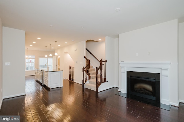 unfurnished living room featuring recessed lighting, stairway, dark wood-type flooring, a fireplace with flush hearth, and a sink