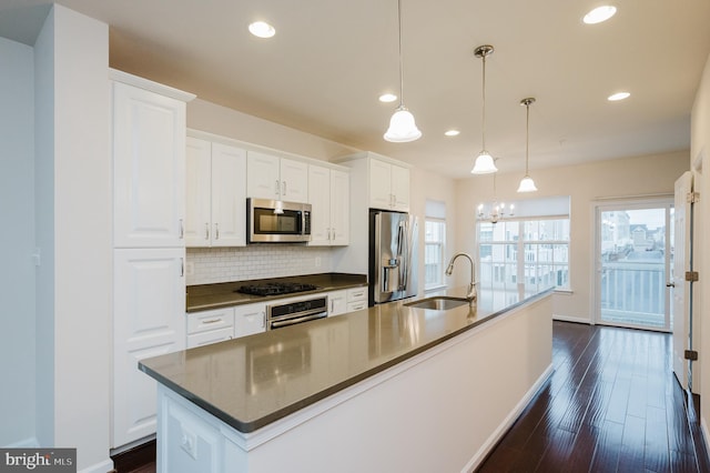 kitchen featuring tasteful backsplash, dark countertops, an island with sink, appliances with stainless steel finishes, and a sink