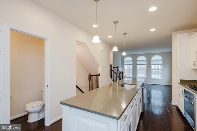 kitchen with dark wood-type flooring, a sink, stainless steel oven, and white cabinets