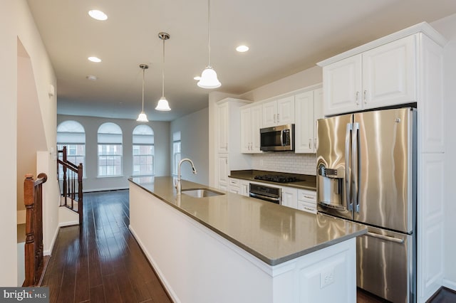 kitchen with dark wood-style flooring, a center island with sink, stainless steel appliances, white cabinets, and a sink