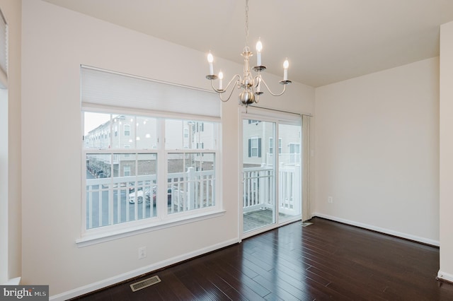 empty room with dark wood-style floors, a notable chandelier, visible vents, and baseboards