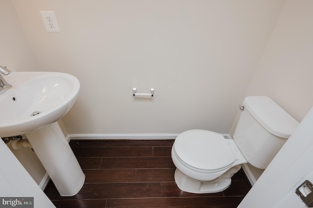 half bath featuring wood finished floors, toilet, and baseboards