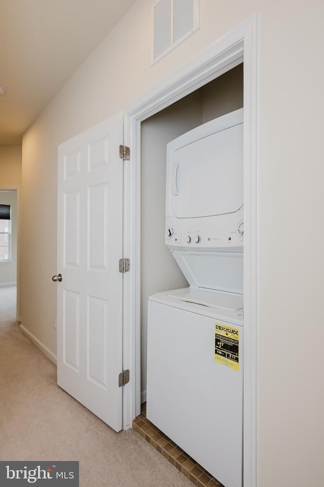 washroom featuring light colored carpet, laundry area, visible vents, baseboards, and stacked washer and clothes dryer