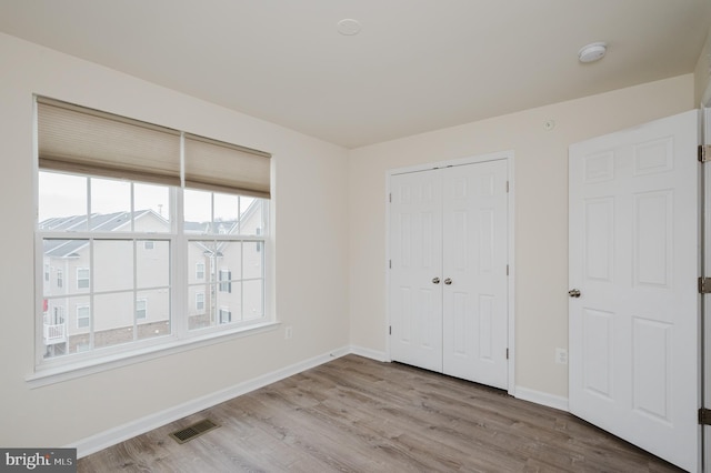 unfurnished bedroom featuring a closet, visible vents, baseboards, and wood finished floors