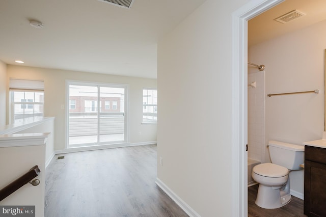 full bath with toilet, plenty of natural light, wood finished floors, and vanity