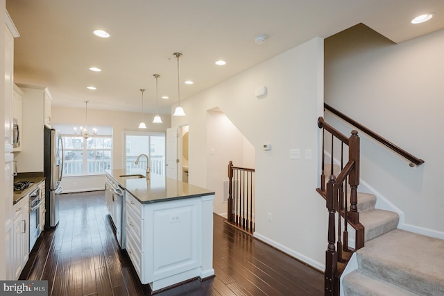 kitchen featuring dark wood-style flooring, a center island with sink, stainless steel appliances, white cabinetry, and a sink