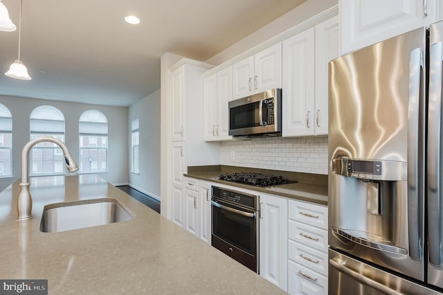 kitchen with stainless steel appliances, a sink, white cabinets, tasteful backsplash, and decorative light fixtures