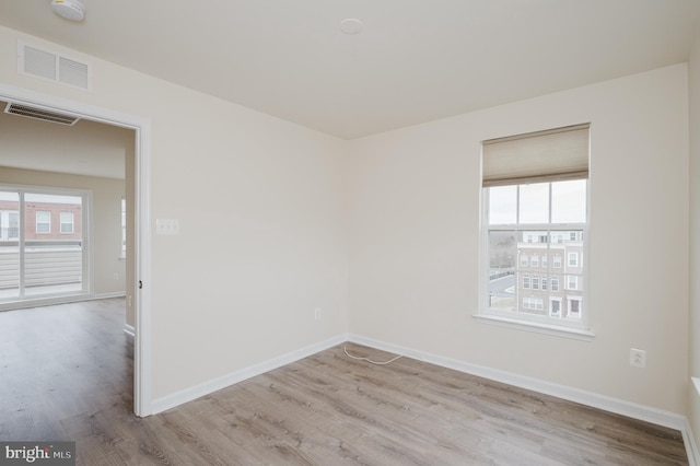 empty room featuring a healthy amount of sunlight, visible vents, and wood finished floors