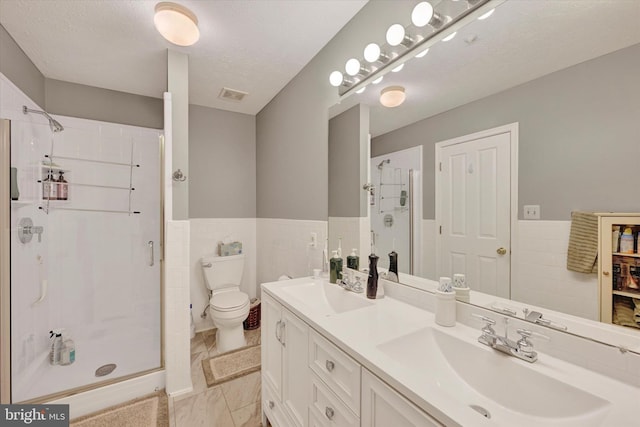 bathroom with vanity, toilet, a textured ceiling, tile walls, and an enclosed shower