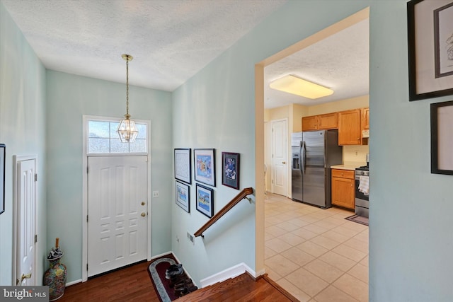 entrance foyer with light wood-type flooring, a textured ceiling, and an inviting chandelier