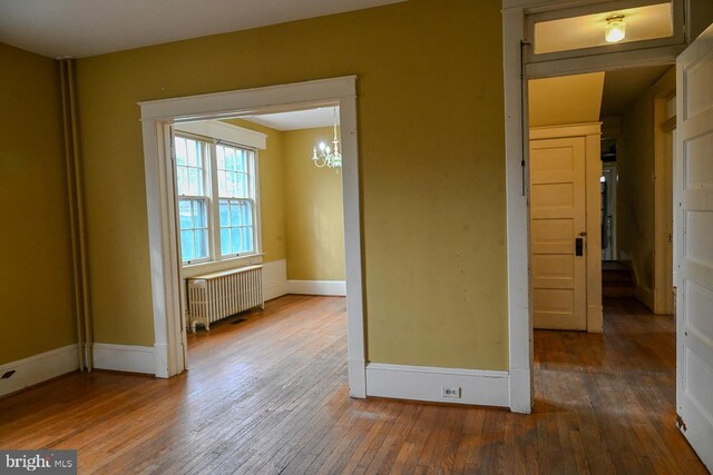 empty room featuring hardwood / wood-style flooring, an inviting chandelier, and radiator