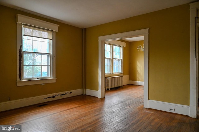 unfurnished room with hardwood / wood-style flooring, a healthy amount of sunlight, radiator heating unit, and an inviting chandelier