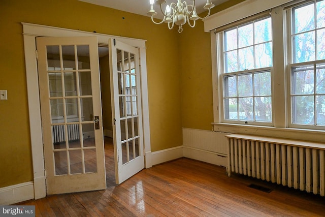 interior space with a notable chandelier, wood-type flooring, and radiator