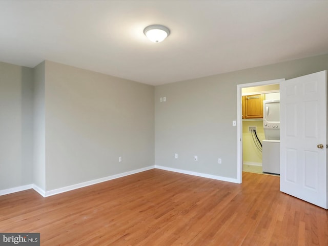 empty room with stacked washer and dryer and light hardwood / wood-style flooring