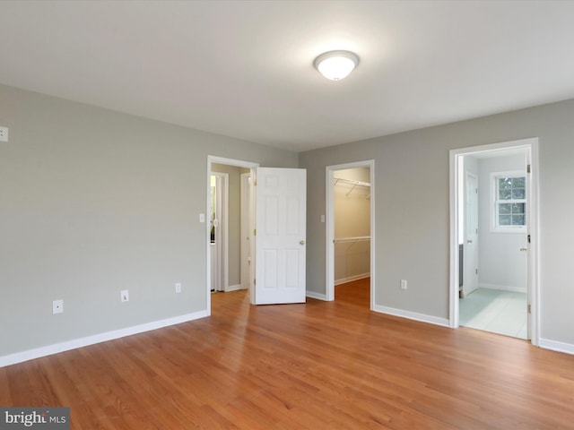 unfurnished bedroom featuring a closet, light wood-type flooring, a spacious closet, and ensuite bath