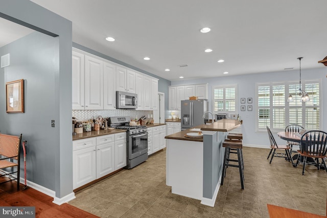 kitchen with a kitchen bar, stainless steel appliances, a kitchen island with sink, white cabinetry, and hanging light fixtures